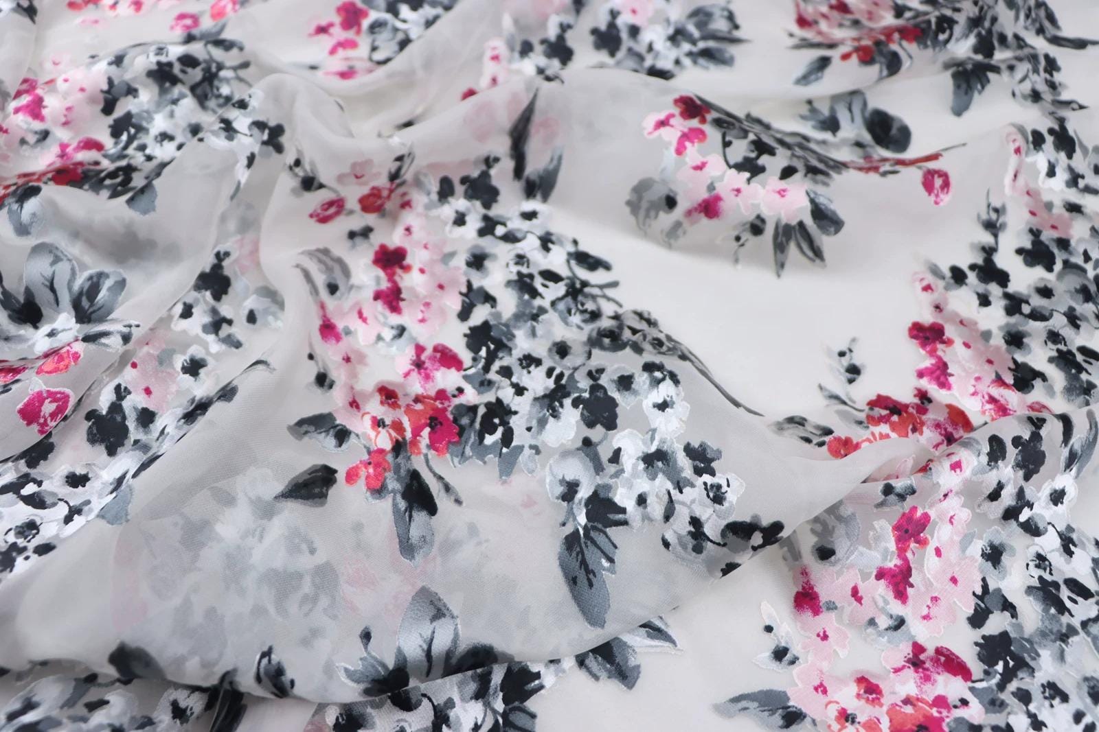 a close-up view of a fabric with a floral pattern in shades of pink and black. The fabric appears to be white, and the pattern consists of various shades of pink and black flowers and leaves. The fabric is crumpled and wrinkled, giving it a soft and delicate appearance.