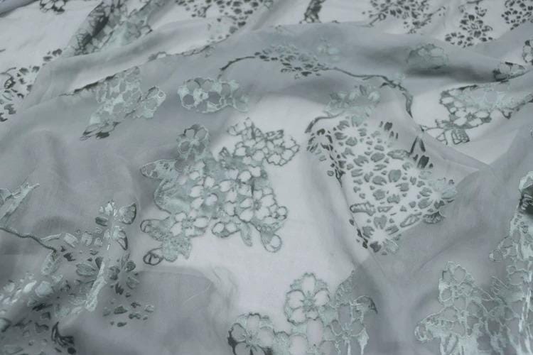 a close-up view of a fabric with a floral pattern, featuring various shades of gray and white.