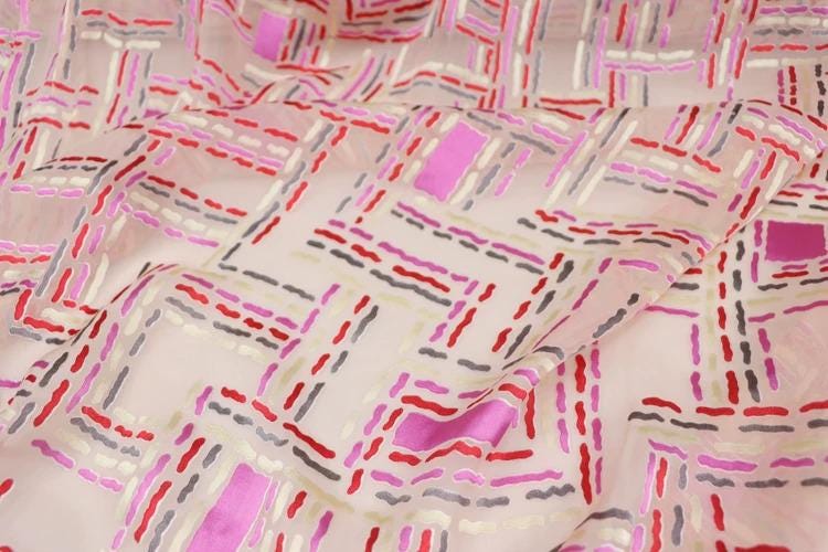 a close-up view of a fabric with a geometric pattern of pink, red, and gray lines and shapes.