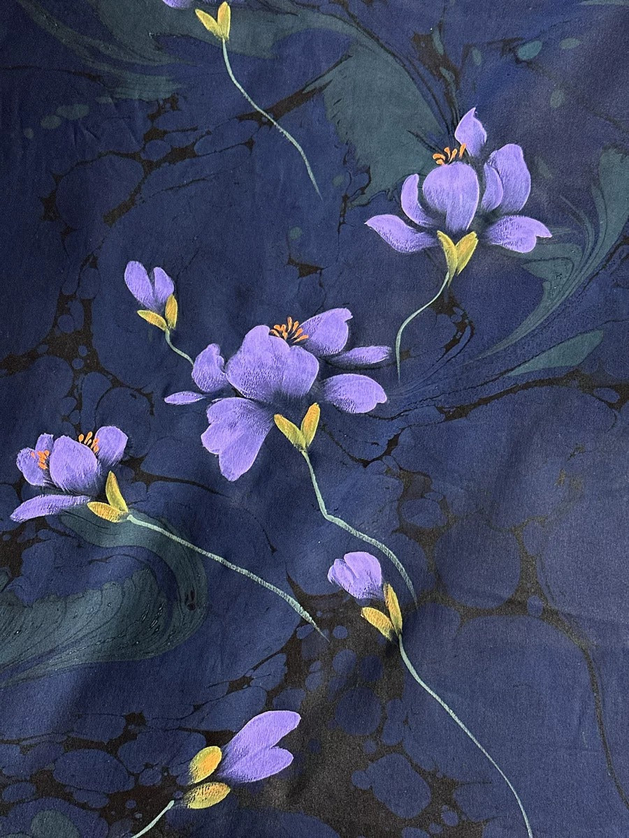 a close-up view of a dark blue fabric with delicate purple flowers and green stems. The flowers are the main focus of the image, with their vibrant colors and intricate details creating a visually striking composition.