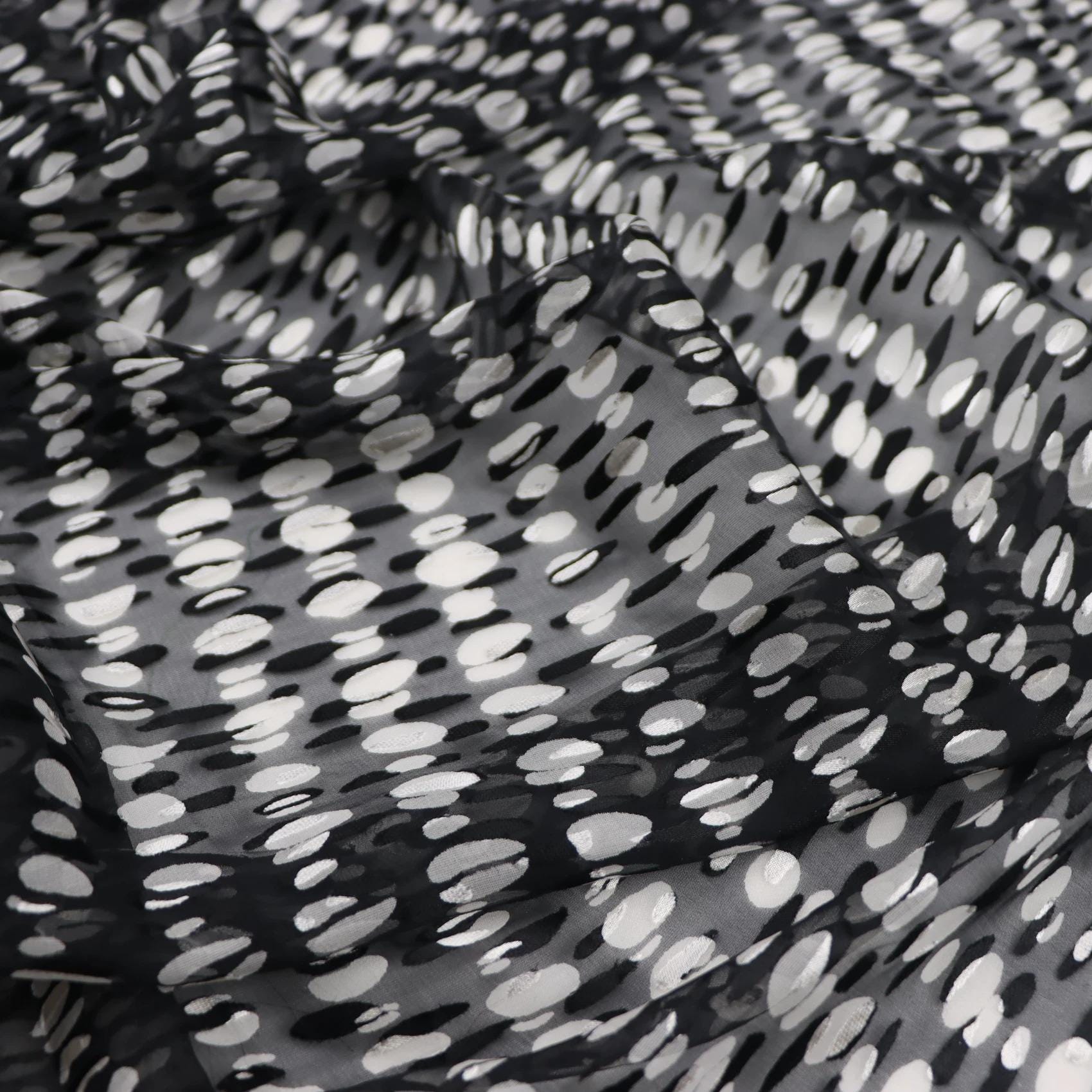 a close-up view of a fabric with a black and white polka dot pattern. The fabric appears to be made of sheer material, with a textured and wrinkled appearance.