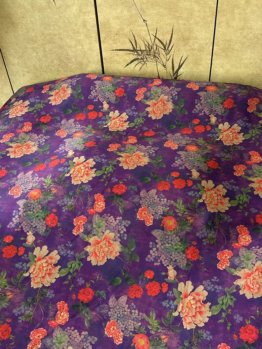 a bed with a purple comforter featuring a floral pattern in shades of red, orange, and white. The comforter is spread out on the bed, creating a visually appealing and colorful display.