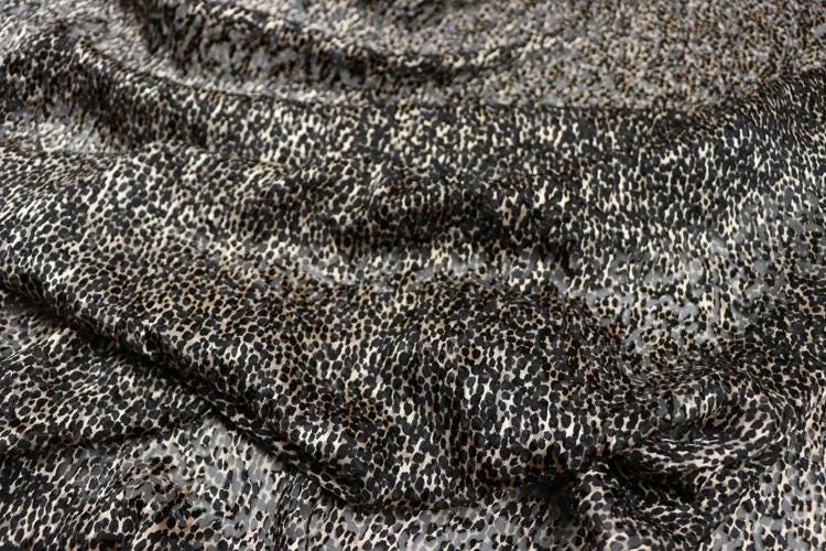 a close-up view of a fabric with a distinctive leopard print pattern. The fabric appears to be a dark-colored material with a mix of black and white spots, resembling the appearance of a leopard's fur. The fabric is crumpled and wrinkled, giving it a textured and somewhat messy appearance.