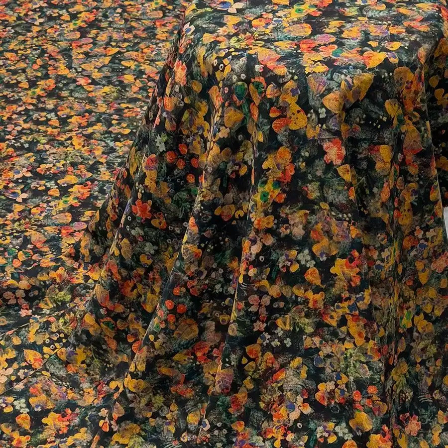 a fabric with a vibrant floral print in shades of orange, yellow, and green. The fabric appears to be a dark-colored material, possibly black or dark green, with a pattern of flowers and leaves covering it. The fabric is spread out, covering a significant portion of the frame, and the colors and patterns create a visually striking and eye-catching display.