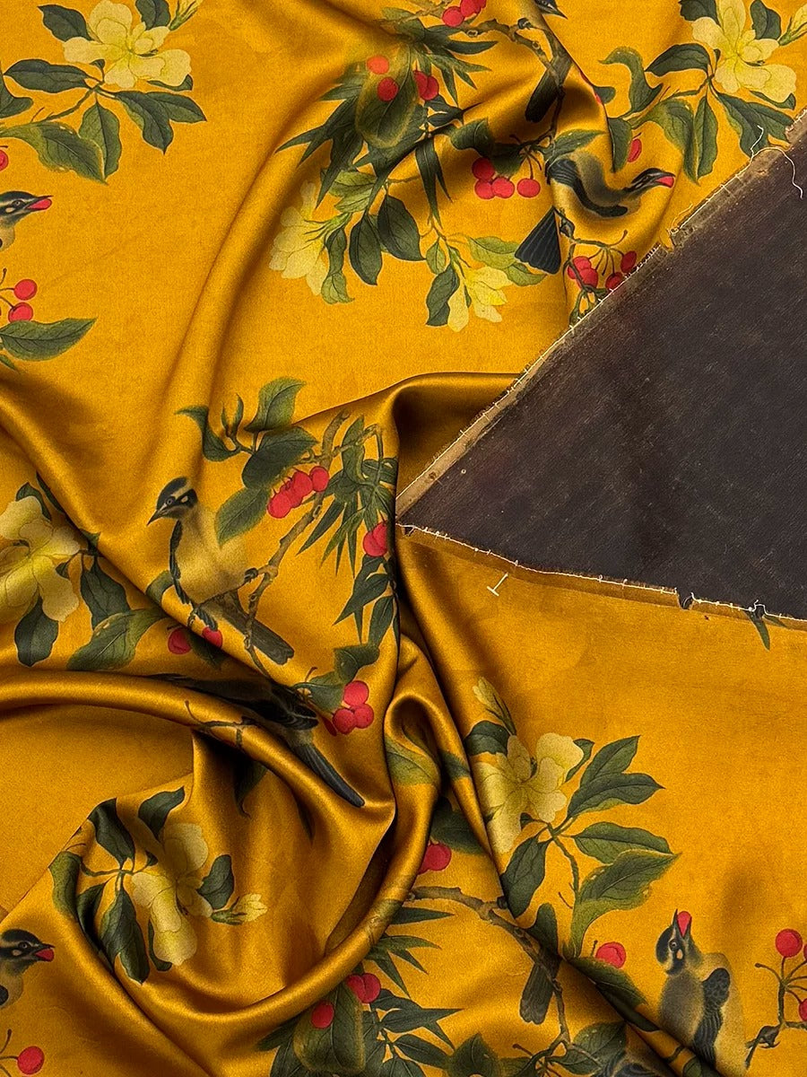 The image is a close-up view of a fabric with a vibrant yellow and green floral pattern, featuring a bird and red berries. The fabric appears to be made of silk or a similar material, and there is a dark fabric or material visible on the right side of the image.