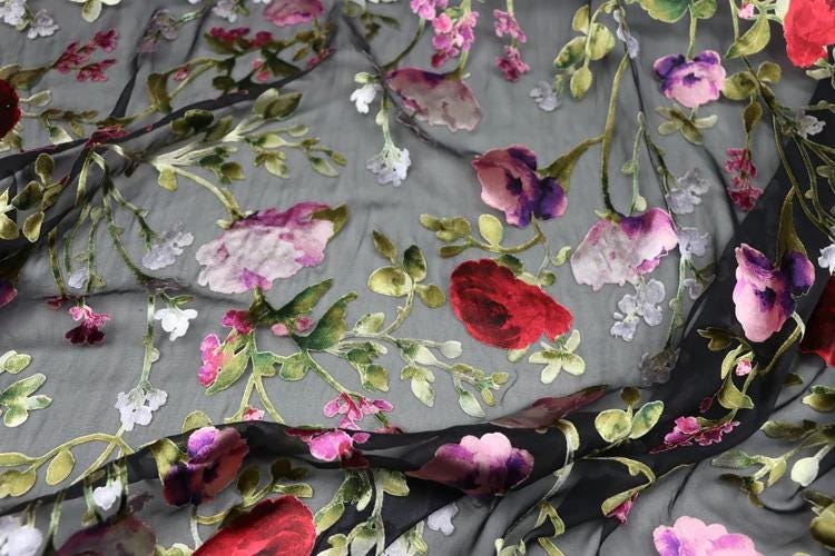 a close-up view of a fabric with a floral pattern, including red, pink, and white flowers. The fabric appears to be a sheer material, with the flowers and leaves creating a visually appealing and intricate design.