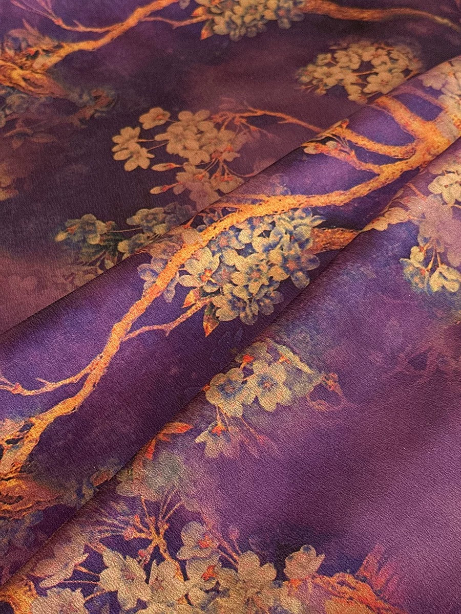 a close-up view of a fabric with a floral pattern in shades of purple and gold. The fabric appears to be a piece of clothing or textile, with the intricate floral design visible on the surface.
