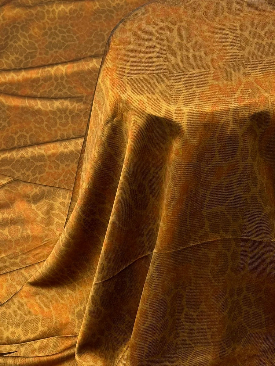a close-up view of a fabric with a leopard print pattern, featuring a warm, earthy color palette of browns and oranges.