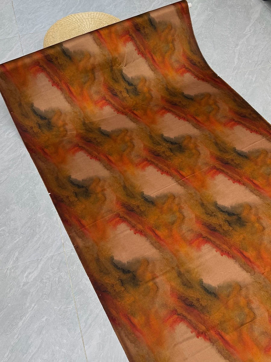 a large piece of fabric with a vibrant, abstract pattern in shades of orange, brown, and black. The fabric appears to be rolled up and displayed on a gray floor, creating a visually striking contrast between the colors and the neutral background.