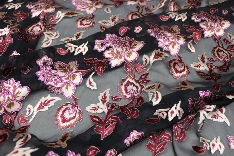 a close-up view of a fabric with a floral pattern in shades of pink, red, and black. The fabric appears to be a sheer material, with the pattern of flowers and leaves visible on the surface.