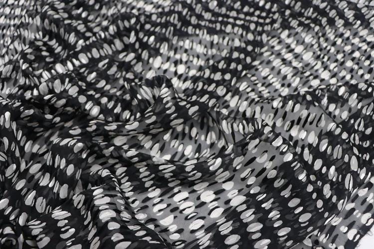 a close-up view of a fabric with a black and white polka dot pattern. The fabric appears to be wrinkled, giving it a textured and slightly crumpled appearance.
