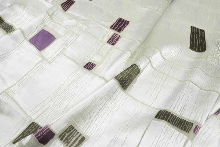 a close-up view of a white fabric with a pattern of purple and gray squares and rectangles.