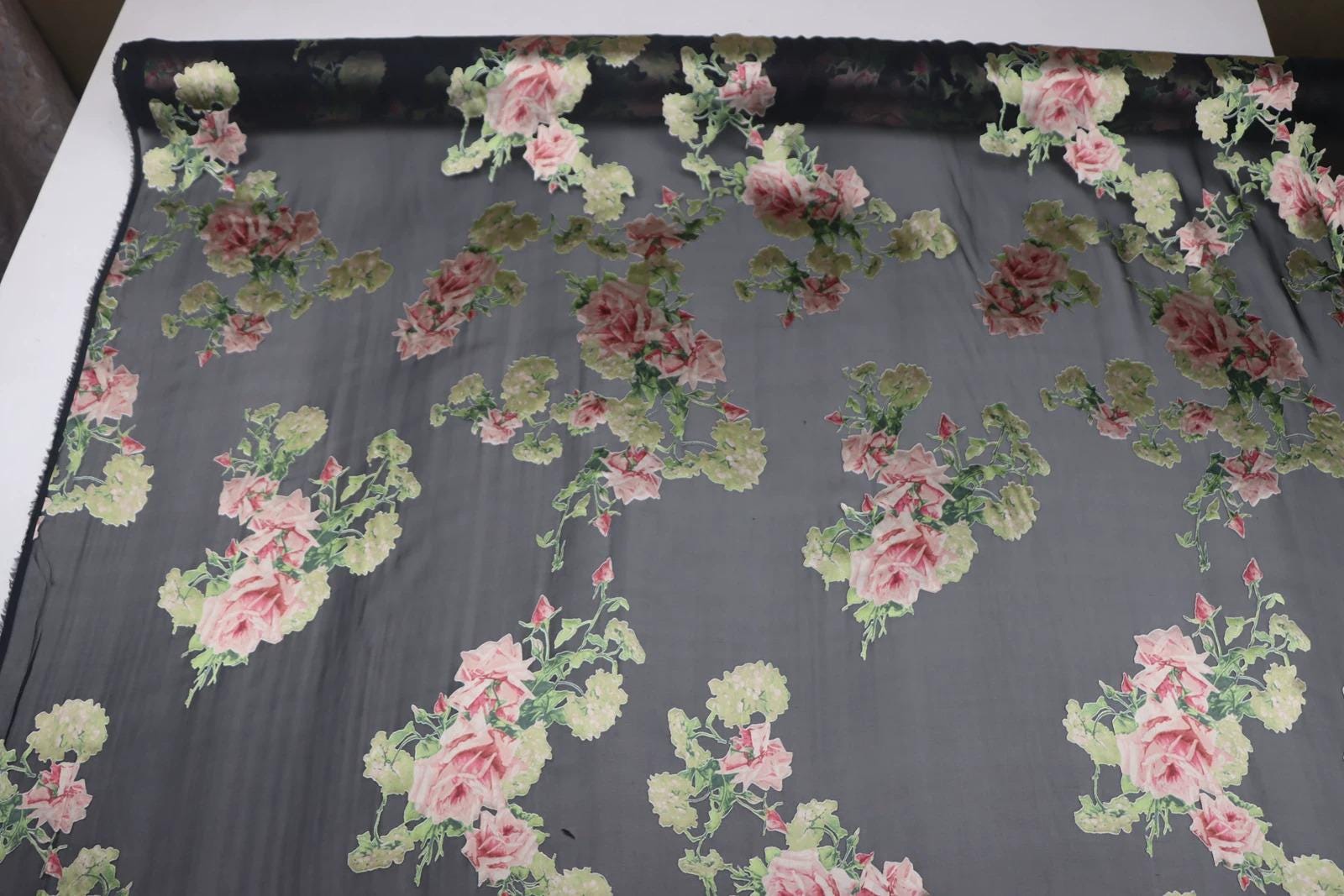 a close-up view of a fabric with a floral pattern, including pink and green flowers. The fabric appears to be a sheer material, with a black border. The pattern is intricate and detailed, showcasing the craftsmanship of the fabric.