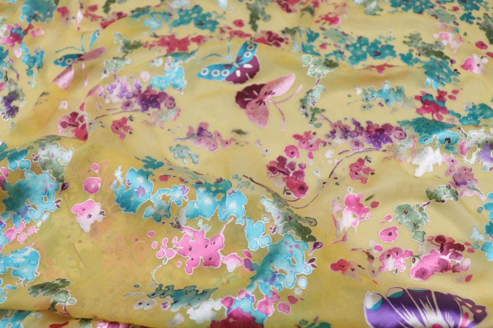 The image is a close-up of a fabric with a vibrant floral pattern, featuring a variety of colorful flowers and butterflies.