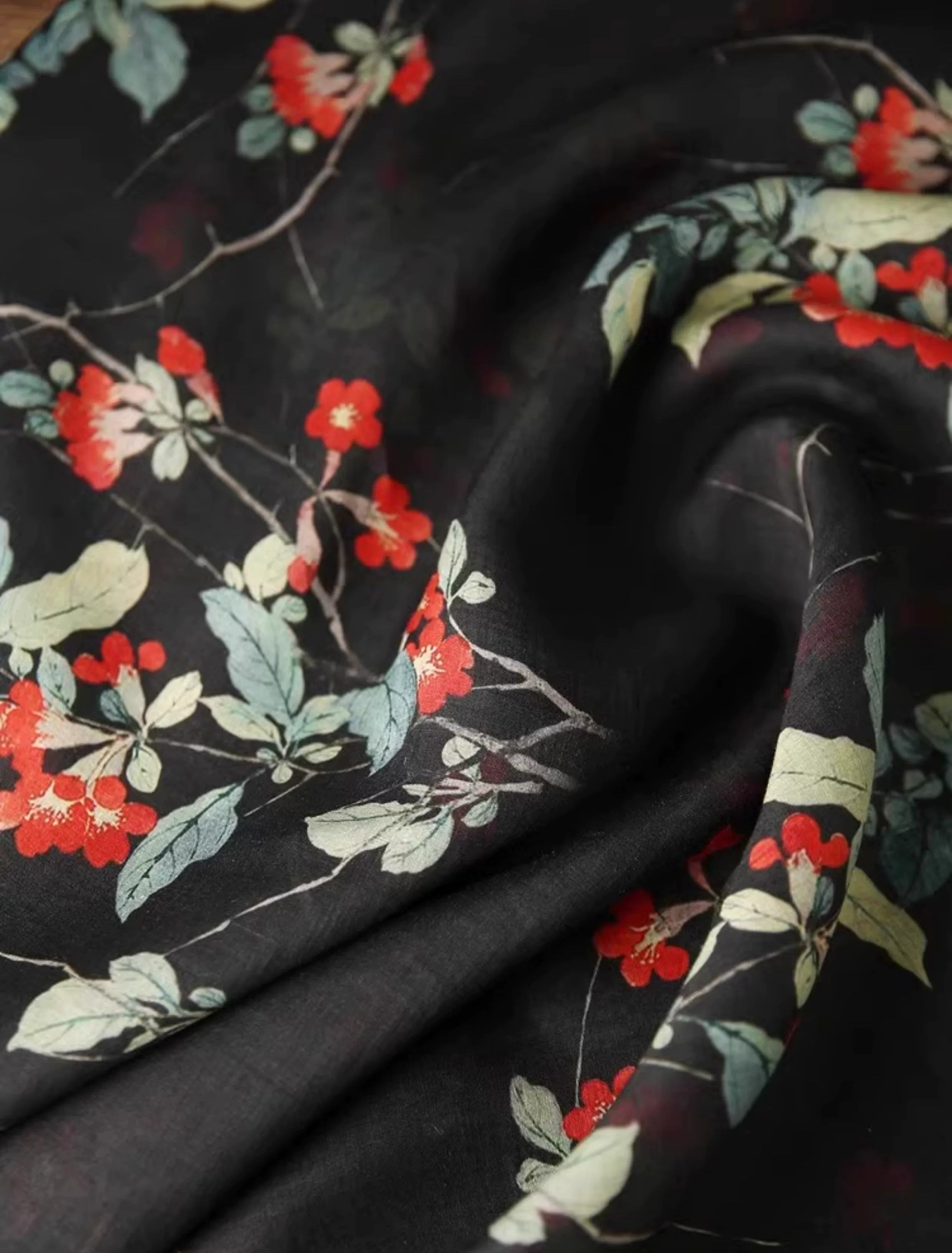 a close-up view of a black fabric with a floral pattern of red flowers and green leaves.