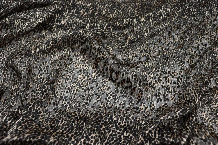 a close-up view of a fabric with a distinctive leopard print pattern. The fabric appears to be a dark-colored material with a mix of black and gray spots, creating a visually striking and textured appearance.