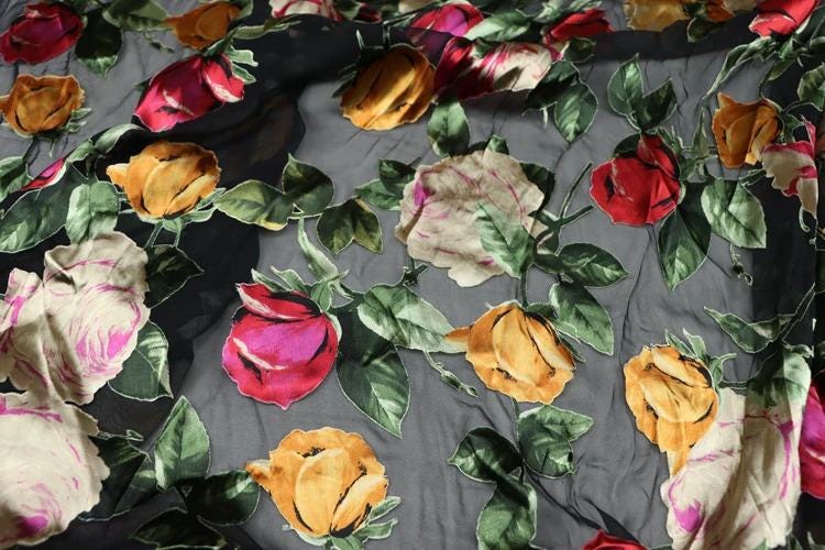 a close-up view of a fabric with a floral pattern of red, orange, and yellow roses against a dark background.