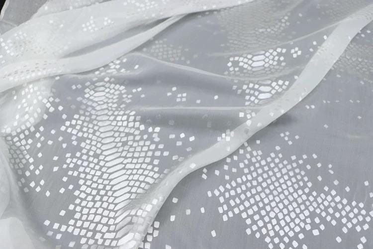 a close-up view of a white fabric with a pattern of small white squares or dots, creating a textured and visually interesting design.