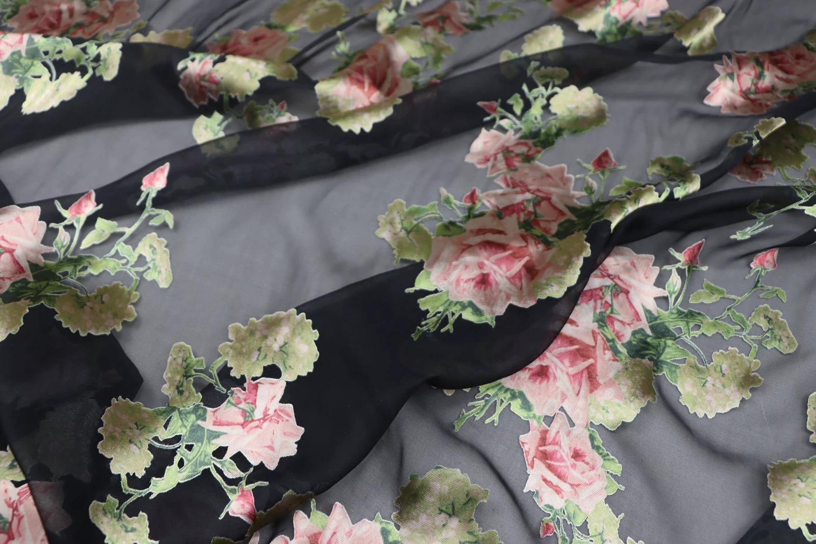 a close-up view of a fabric with a floral pattern, featuring pink and green flowers against a dark background.