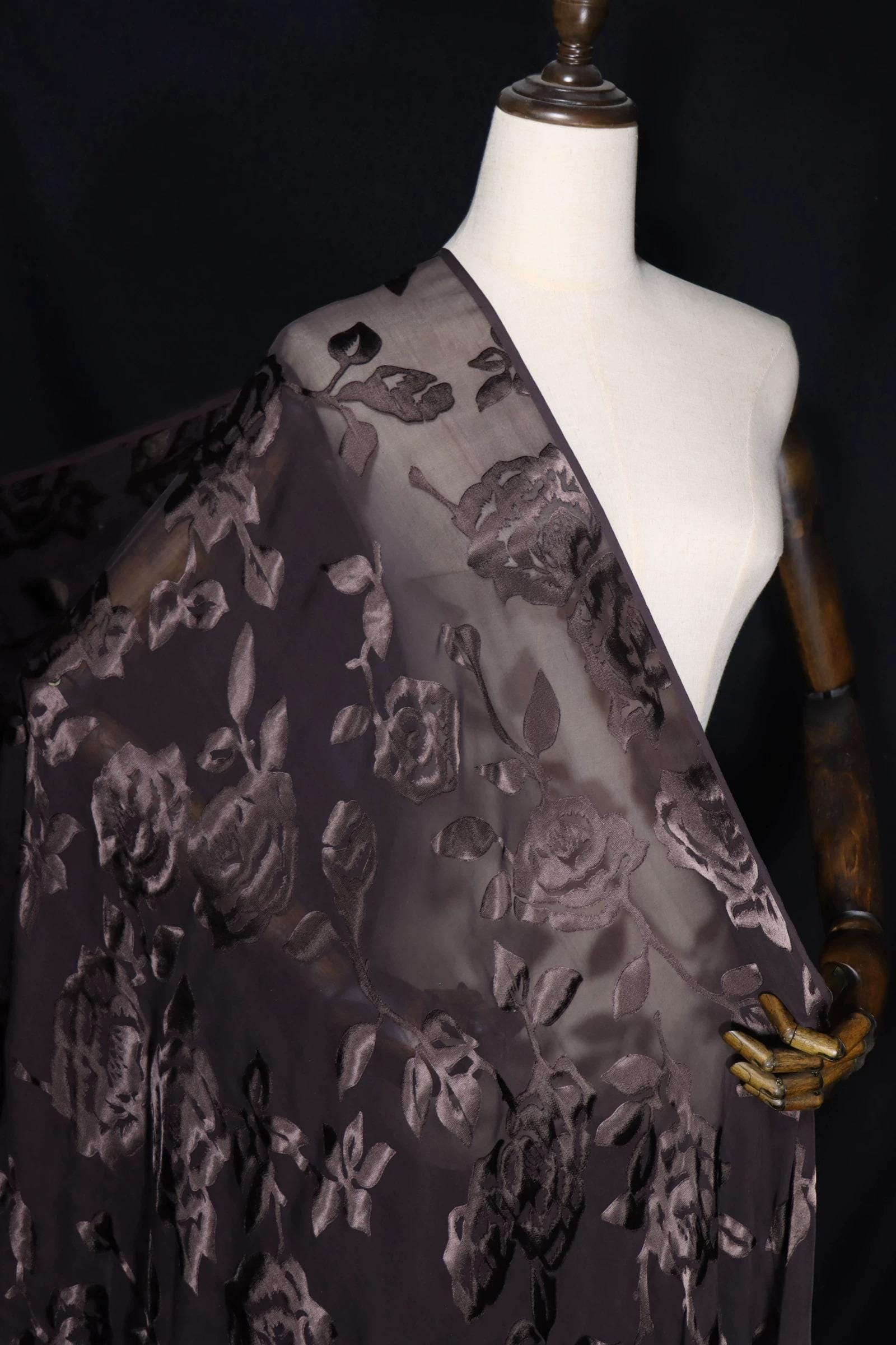 A mannequin wearing a dark purple fabric with a floral pattern, displayed against a dark background.