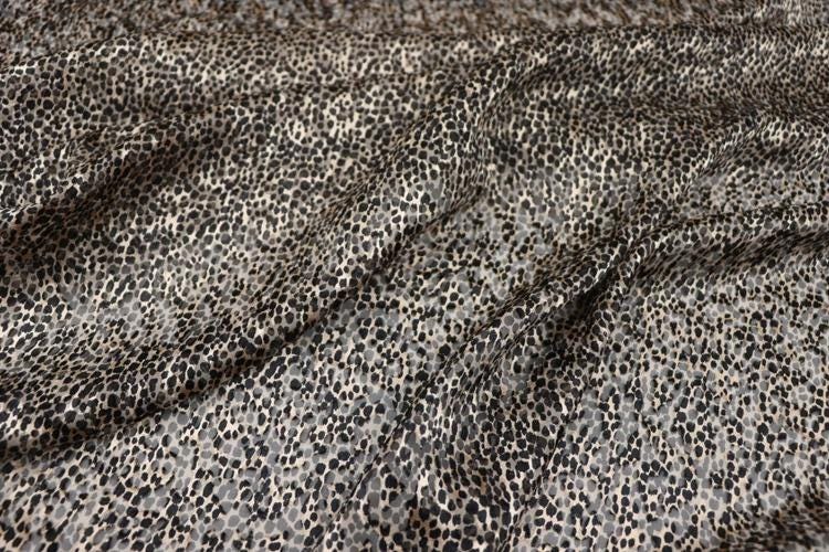 a close-up view of a fabric with a distinctive leopard print pattern. The fabric appears to be made of a material with a textured surface, resembling the appearance of a cat's fur. The pattern consists of small, irregularly shaped dots in shades of black and gray, creating a visually striking and unique design.
