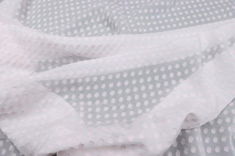 A close-up view of a fabric with a white polka dot pattern, featuring a crumpled texture.