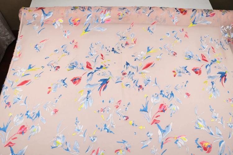 a fabric with a floral pattern in shades of pink and blue. The pattern consists of various flowers and leaves, creating a vibrant and colorful design.