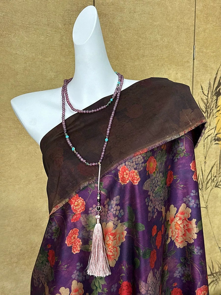 A mannequin wearing a brown shawl with a floral print and a necklace with purple beads and a tassel.
