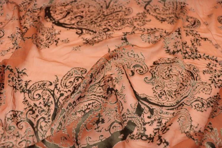 a close-up view of a fabric with a paisley pattern in shades of orange and black. The fabric appears to be wrinkled, giving it a textured and intricate appearance.