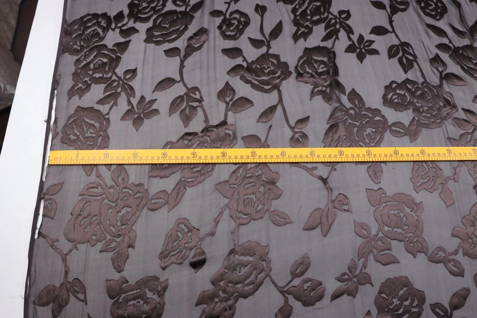 a close-up view of a fabric with a floral pattern, featuring a yellow measuring tape placed across it.