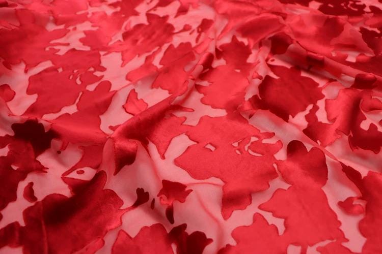a close-up view of a fabric with a red floral pattern. The fabric appears to be made of a shiny, shiny material, possibly silk or satin, and has a slightly wrinkled texture. The pattern consists of red flowers or leaves, which are the main design element of the fabric. The image does not contain any text or other objects, and the focus is solely on the fabric and its floral pattern.