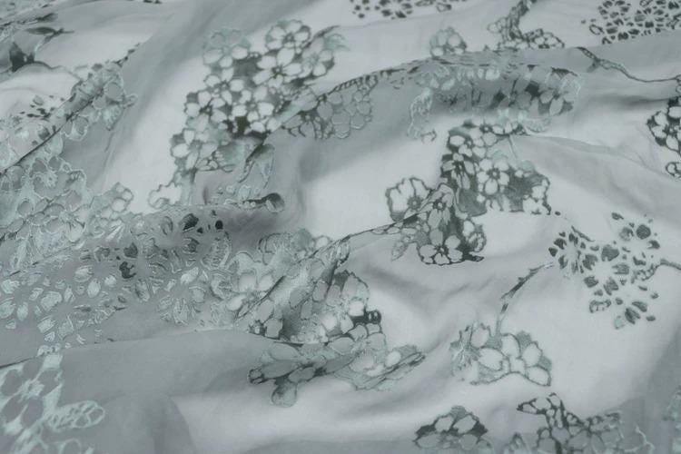 a close-up view of a fabric with a floral pattern, featuring various shades of gray and white.