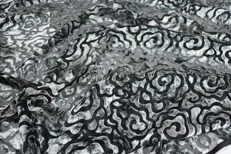 a close-up view of a fabric with a black and white pattern, featuring a repeating swirl or wave-like design.