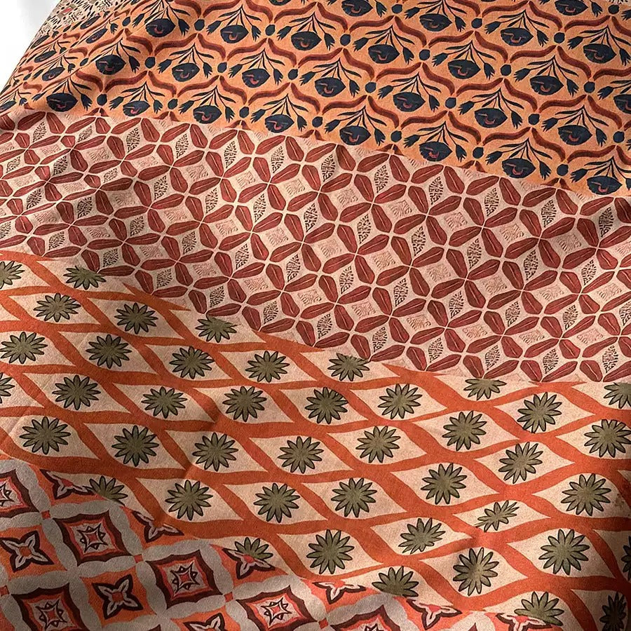 The image is a close-up view of a fabric with a repeating pattern of orange and green floral designs. The pattern consists of various shapes and sizes of flowers and leaves, creating a visually appealing and intricate design.