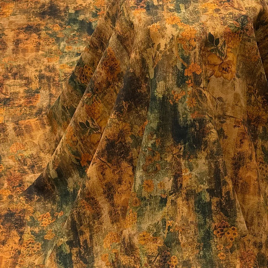 a close-up view of a fabric with a floral pattern in shades of orange and green. The fabric appears to be folded or draped, creating a textured and visually interesting surface.