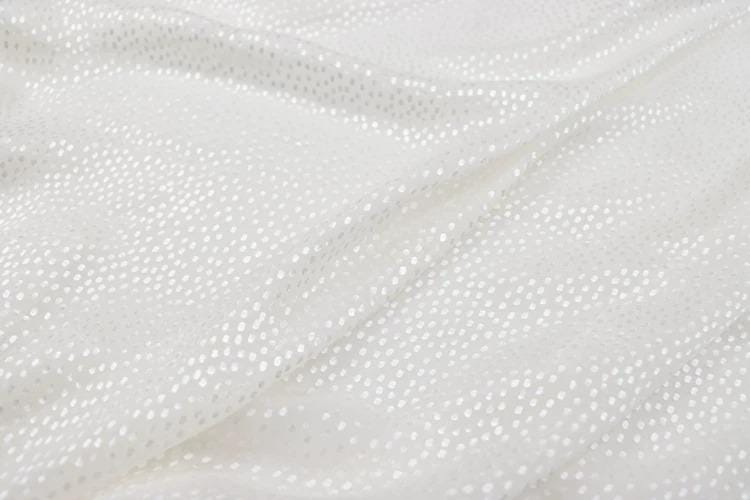 a close-up view of a white fabric with small white dots or polka dots, creating a textured and shiny appearance.