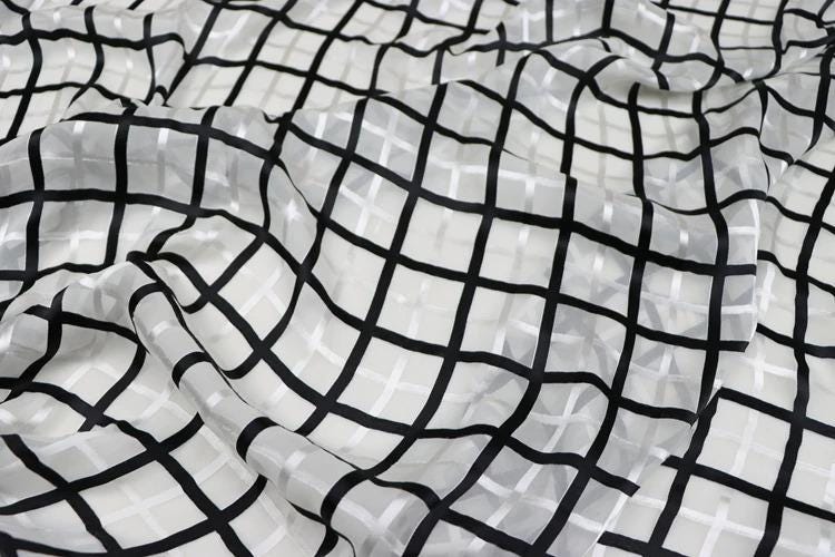 a close-up view of a fabric with a black and white checkered pattern. The fabric appears to be made of a sheer material, with a grid-like design that creates a visually striking and textured appearance.