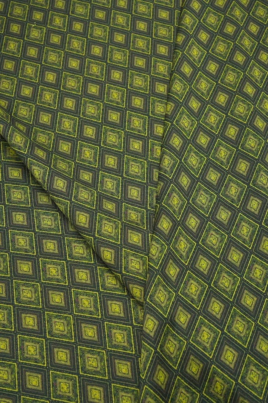 a close-up view of a fabric with a repeating pattern of green and black squares. The pattern is composed of small squares arranged in a diagonal grid-like design, creating a visually striking and intricate design.