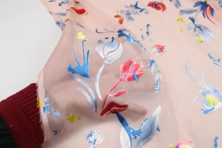A close-up view of a fabric with a floral pattern, featuring various shades of pink, blue, and yellow flowers and leaves.