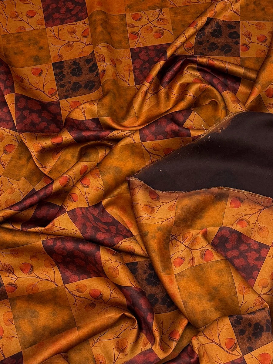 a close-up view of a fabric with a vibrant, colorful pattern of squares and rectangles in shades of orange, brown, and black. The fabric appears to be made of silk or a similar material, and it has a crinkled texture, giving it a soft and luxurious appearance.