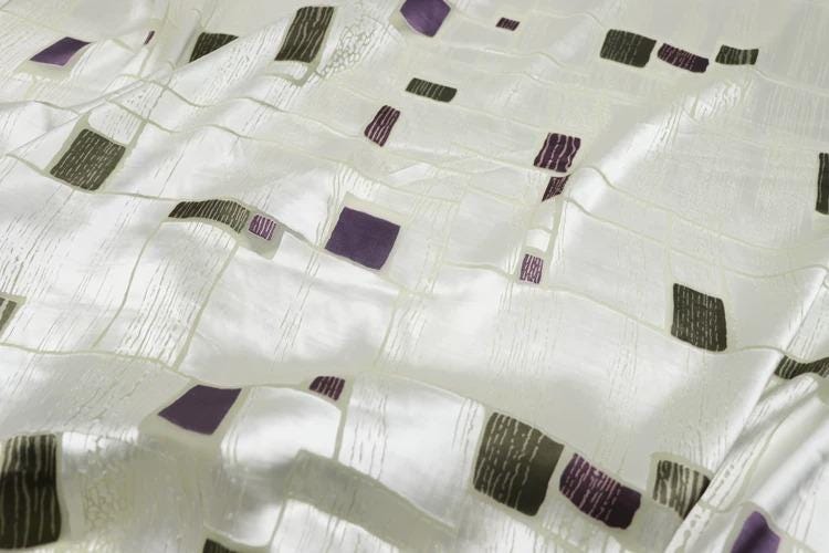 a close-up view of a white fabric with a pattern of purple and black squares and rectangles.