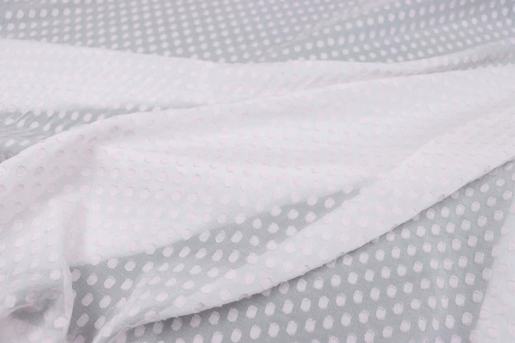 a close-up view of a fabric with a white polka dot pattern. The fabric appears to be a sheer material, with a light gray background. The pattern consists of small white dots arranged in a diagonal line across the fabric, creating a textured and visually interesting appearance.