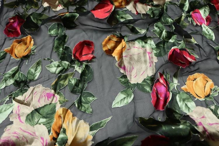 a close-up view of a fabric with a floral pattern, including red, pink, and yellow flowers interspersed with green leaves.