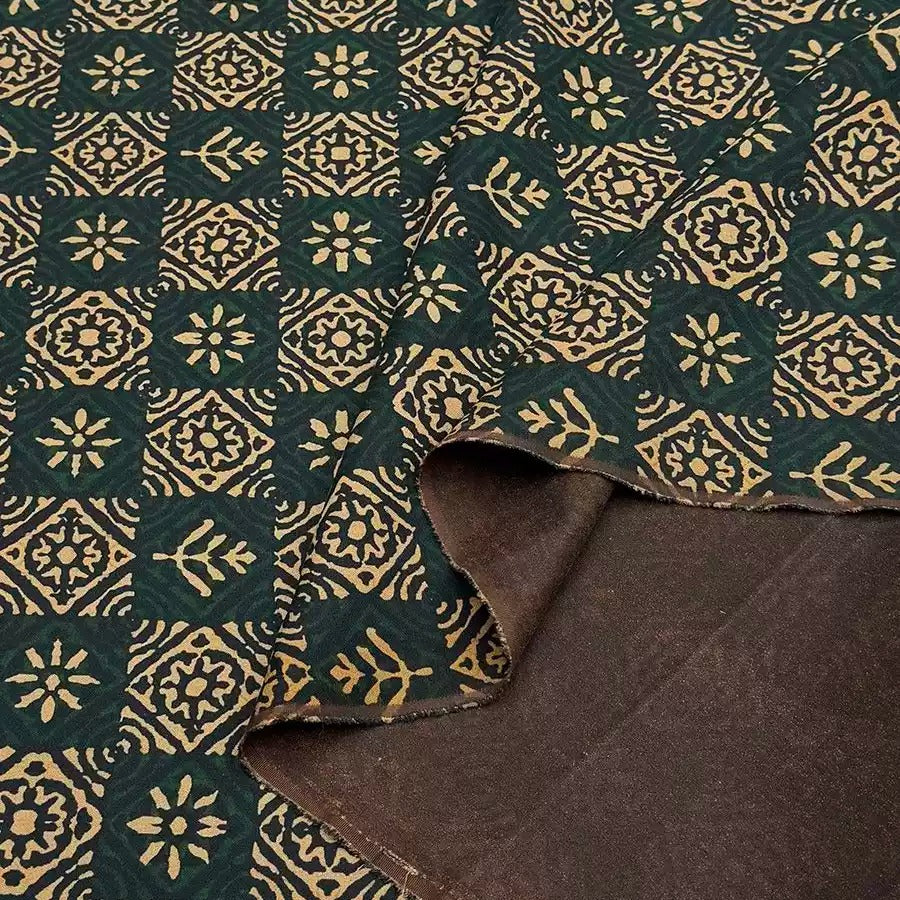a close-up view of a fabric with a repeating pattern of green and gold floral designs. The fabric appears to be made of a dark-colored material, possibly cotton or linen, with a lighter green color. The pattern is intricate and detailed, with the flowers and leaves arranged in a symmetrical and visually appealing manner.