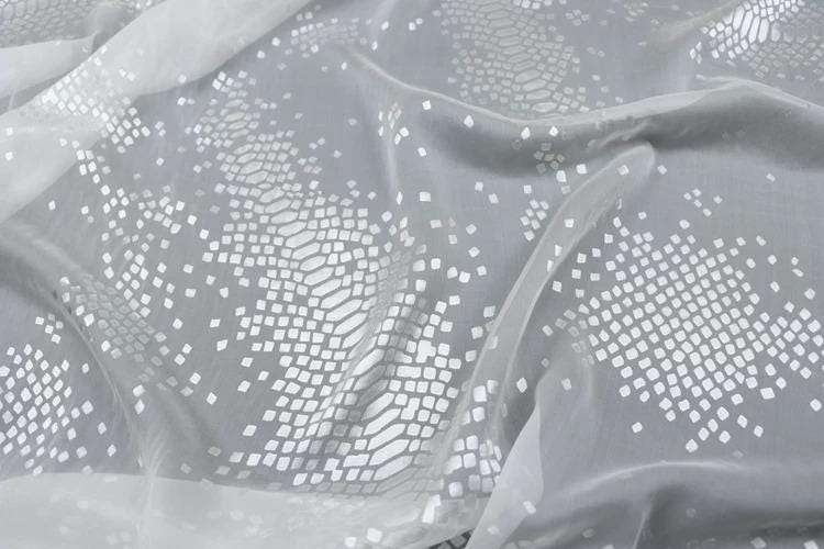 a close-up view of a fabric with a white, diamond-shaped pattern. The fabric appears to be made of a soft, flowing material, possibly silk or chiffon. The pattern consists of numerous small white diamonds arranged in a repeating geometric design, creating a visually striking and intricate appearance.
