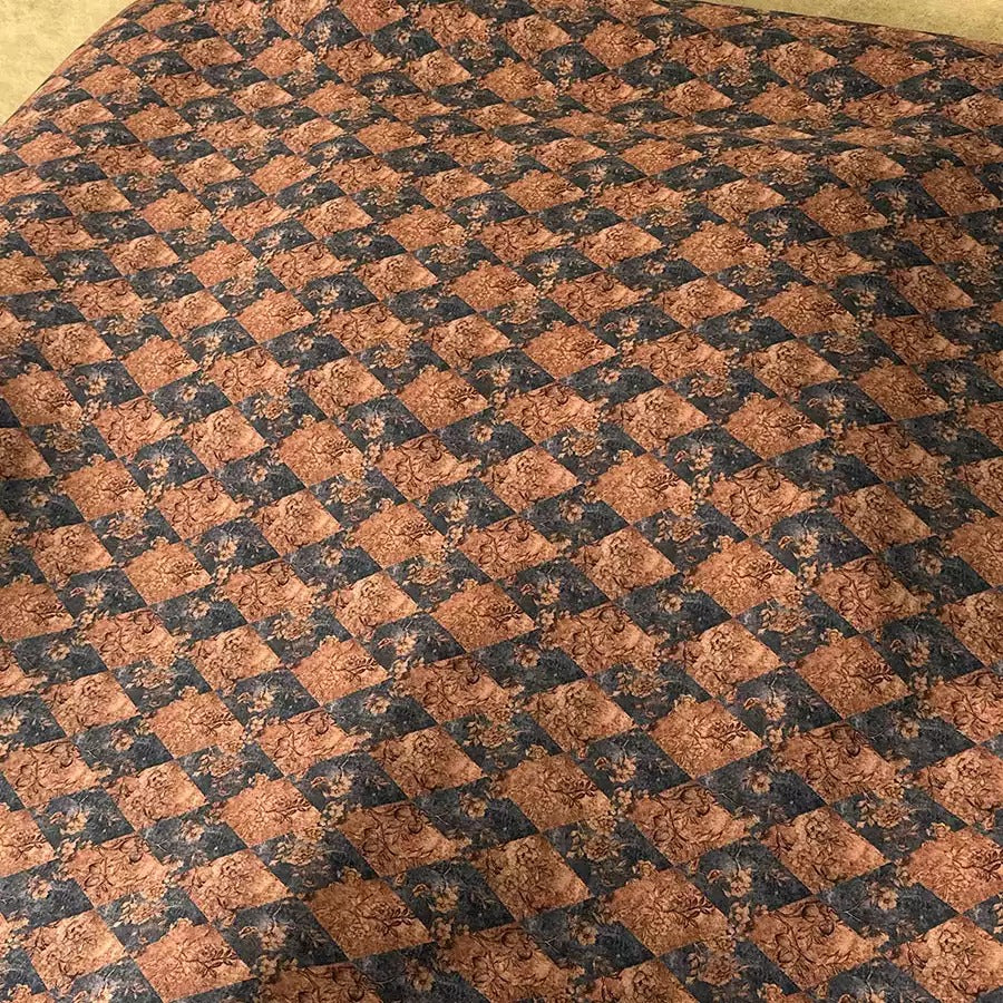 a close-up view of a fabric with a repeating pattern of brown and black diamond shapes. The pattern is intricate and detailed, creating a visually striking design.