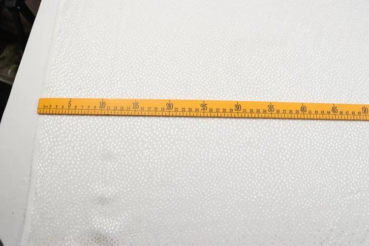 a yellow measuring tape extended across a white fabric with small dots, indicating the size of the fabric.