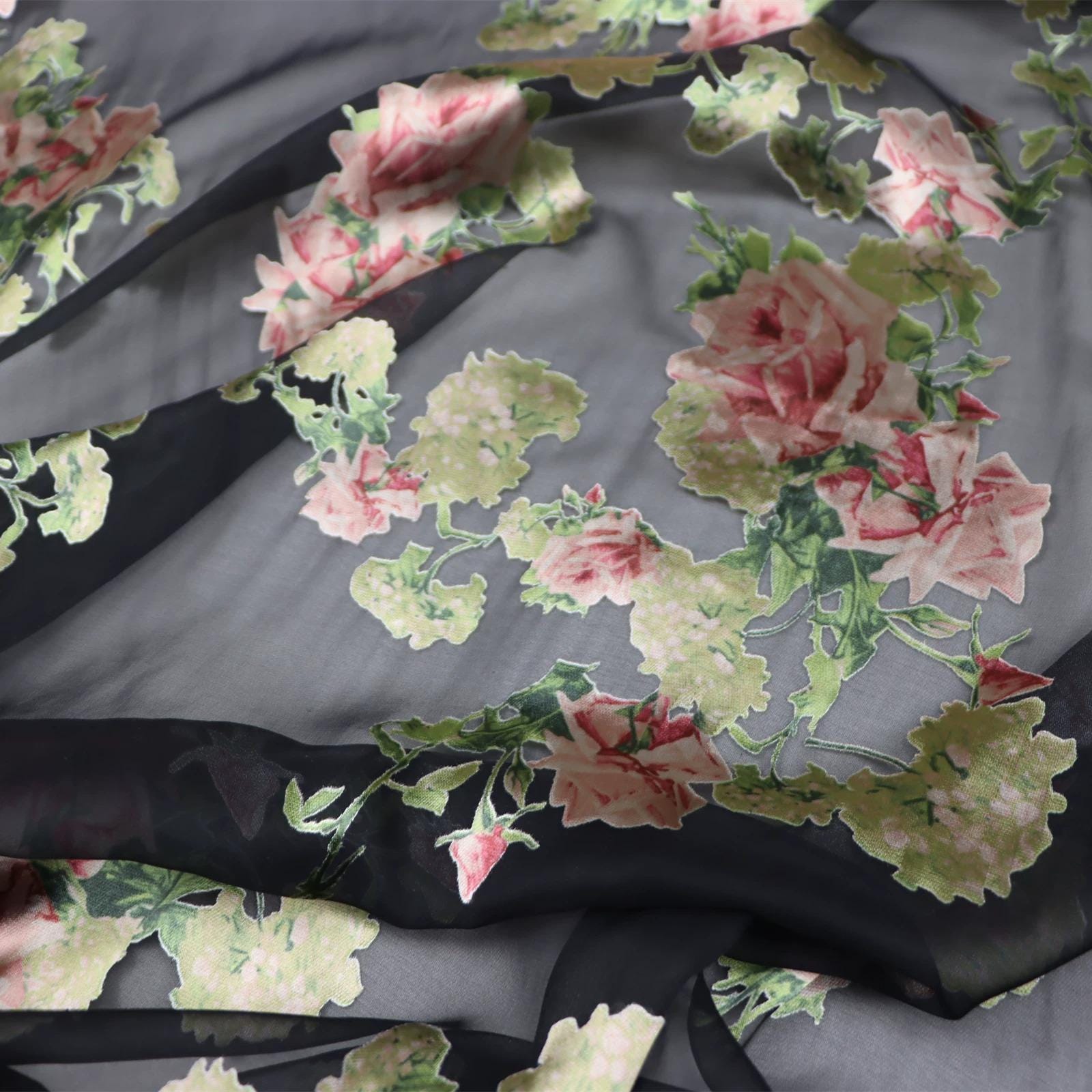 a close-up view of a fabric with a floral pattern, featuring pink and green flowers against a dark background.