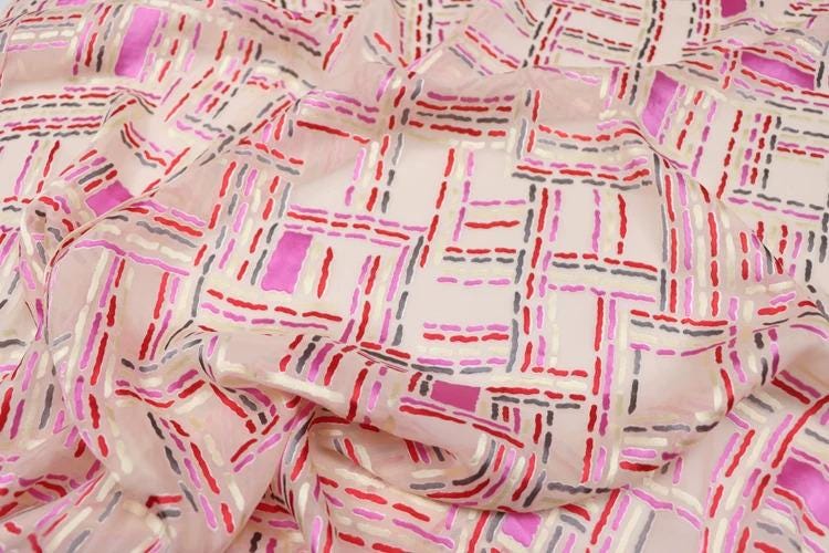 a close-up view of a fabric with a geometric pattern of pink, red, and gray lines and shapes.
