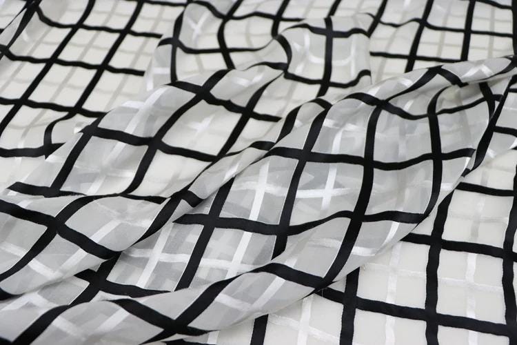 a close-up view of a fabric with a black and white checkered pattern. The fabric appears to be made of a sheer material, with a grid-like design that creates a visually striking pattern.